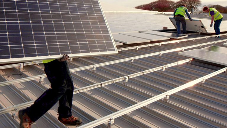Several workers are installing solar panels on a roof